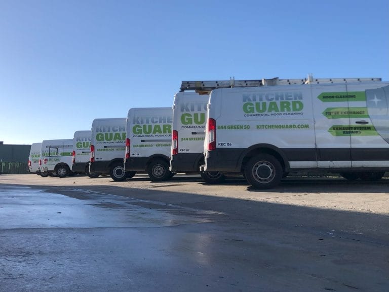 A fleet of white Kitchen Guard vans parked in a parking lot.
